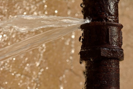 Water spraying out of a rusty, leaking pipe against a blurred background.