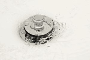 %Title% | 24/7 Rooter &Amp; Plumbing Water swirling around a metallic sink drain stopper, with bubbles and ripples visible on the surface.