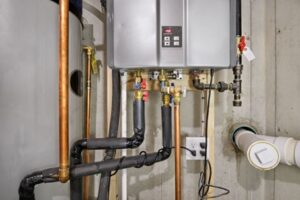 %Title% | 24/7 Rooter &Amp; Plumbing A tankless water heater is mounted on a basement wall, with various copper and insulated pipes connected to it.
