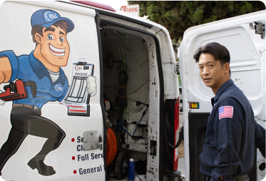 %Imagetitle% | 24/7 Rooter &Amp; Plumbing A plumber stands by an open work van displaying a cartoon plumber graphic, tools, and an American flag patch on his uniform sleeve.
