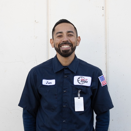 Meet the Team: A man wearing a navy work shirt with a name tag, company logo, and an American flag patch stands smiling in front of a white wall.